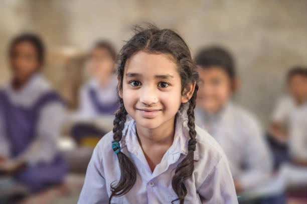 Girl sitting on the floor of her government primary school in uniform along with some of her class mates sitting behind her.  Selective focus, shallow depth of field.